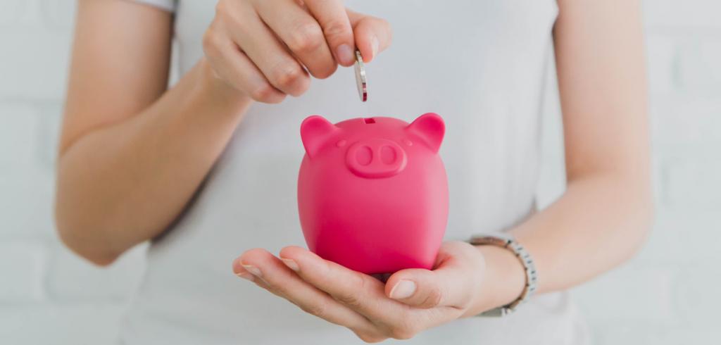 Woman's hand placing coin into piggy bank Woman's hand placing coin into piggy bank